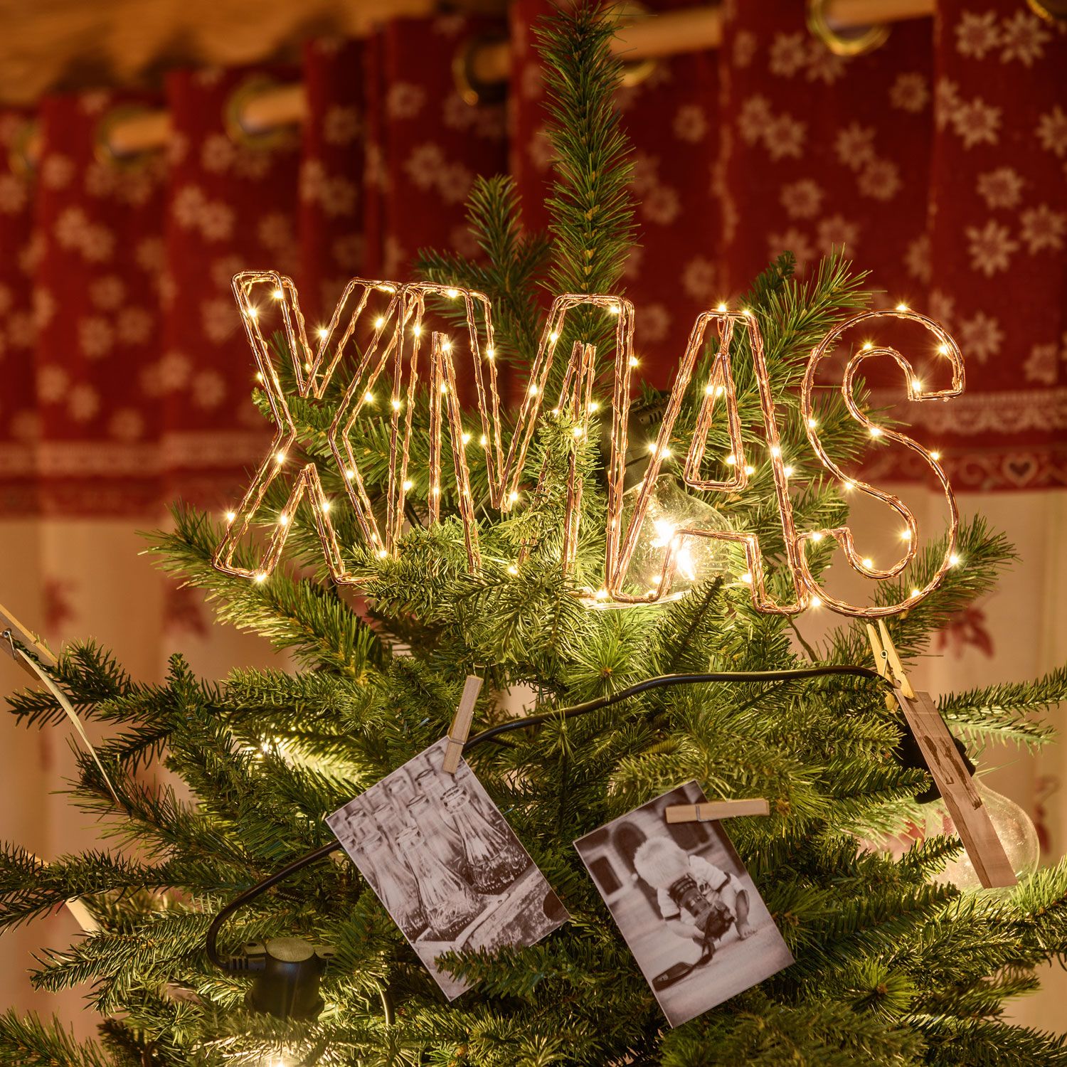 Scritta luminosa XMAS fissata tra i rami in cima a un albero di Natale